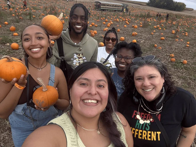 Six ELPA students smile for a selfie in the pumpkin fields at Schuster's Farm. Three of the students are holding small pumpkins that they picked in the field.