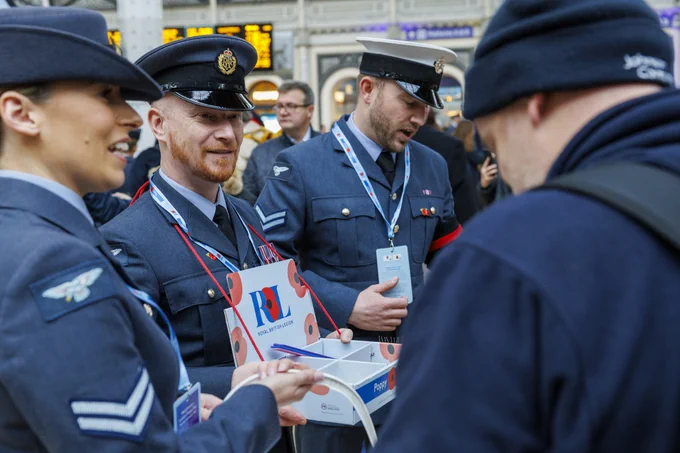 RAF personnel dressed in their blue uniform speaking with members of the public. They have RBL poppy boxes hanging on their chest.