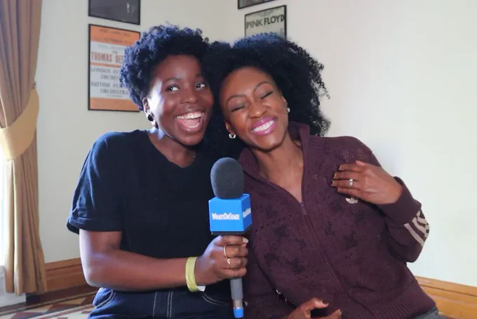 A photo showing two women embracing and holding a microphone 