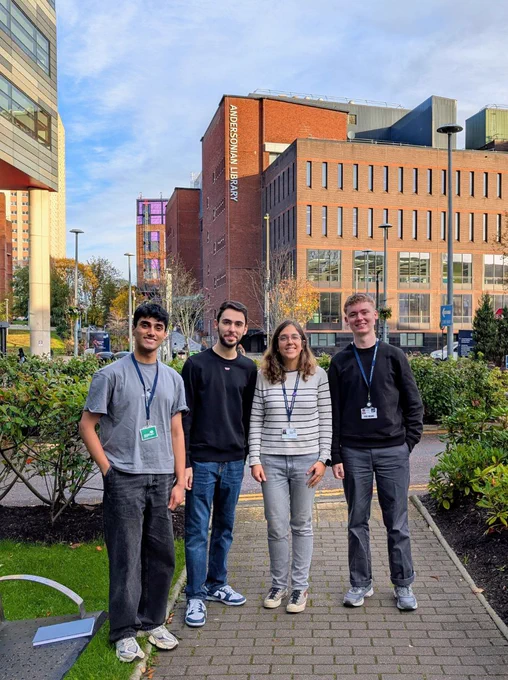 The image shows four people standing at the campus of the University of Strathclyde, with the Andersonian Library building in the back.