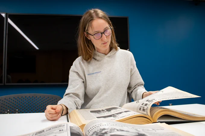 A person sits at a table looking at a bound copy of a newspaper