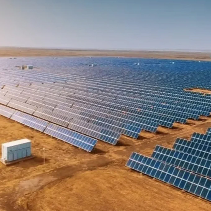 Vast solar farm with numerous photovoltaic panels spread across a flat, arid landscape under a clear sky.