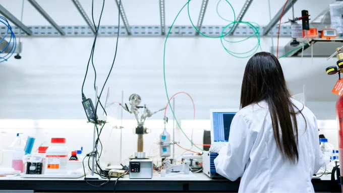 A person with long hair is seen from behind working in a laboratory