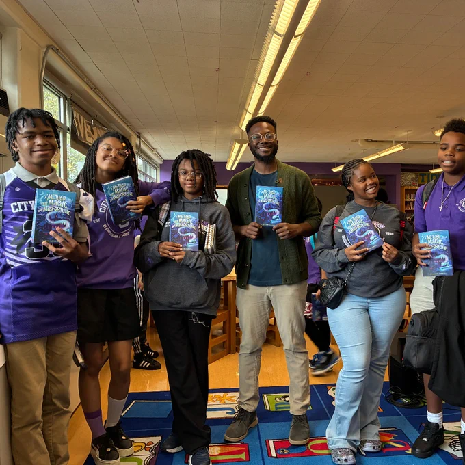 A group of six students and author Craig Kofi Farmer standing in a library holding copies of the book 'Method Magic and Misfortune'.
