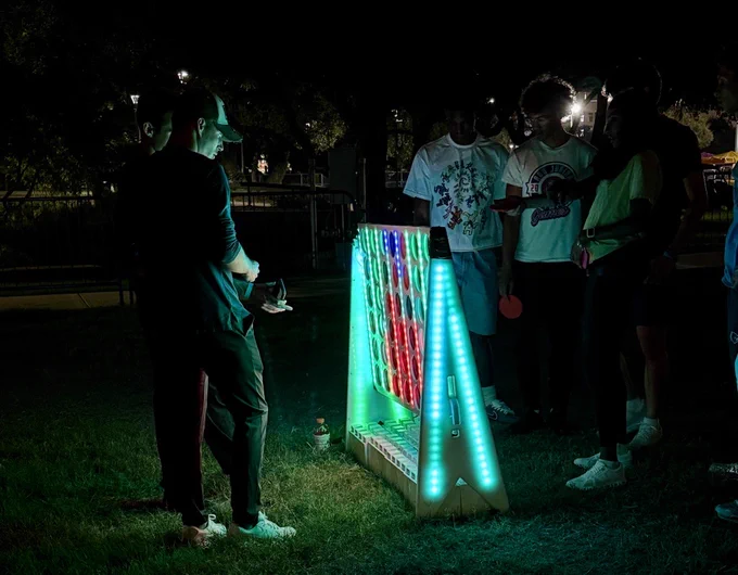 Group of people playing a nighttime game of LED-lit connect 4.