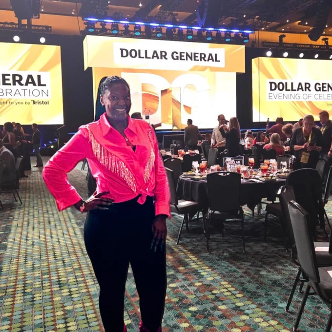 A woman poses in front of a "Dollar General" backdrop at an event. 