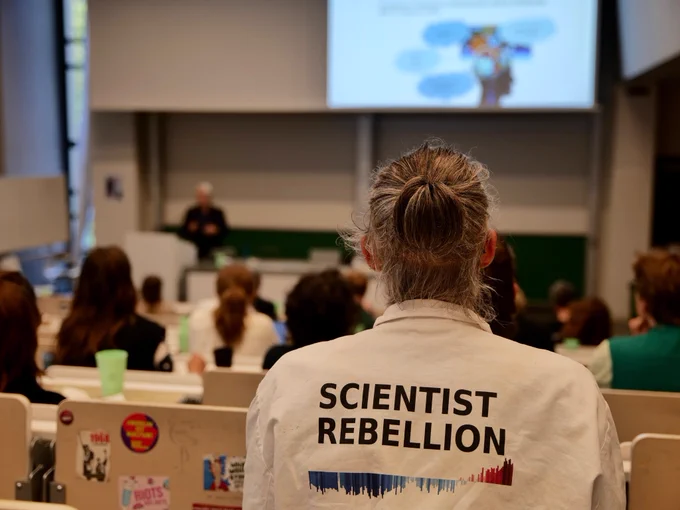 SR activist in lab coat sitting in lecture hall at the Scientists Responsibility summit