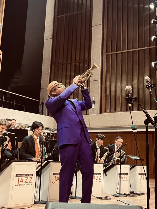 A musician in a purple suit plays a trumpet solo on stage with the Jazz Orchestra in the background.