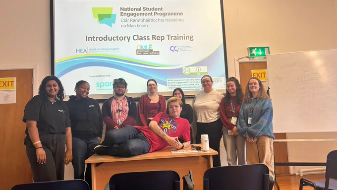 Student trainers Elle and Ebere with class reps in Carlow College after a training session. They are standing in front of a projection screen and smiling.