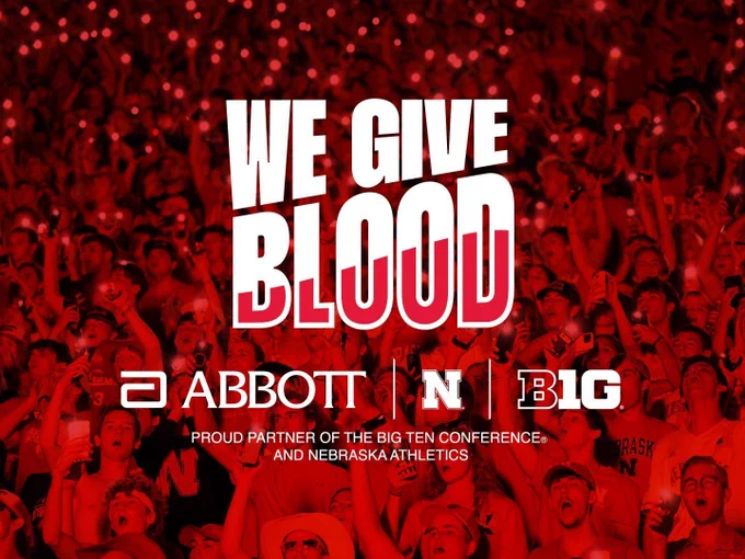 Crowd of Husker fans in the background. Red overlay with text saying, "We Give Blood." Logos of Abbott, UNL, and the Big 10 lined up beneath that. At the very bottom reads, "Proud partner of the Big Ten Conference and Nebraska Athletics."
