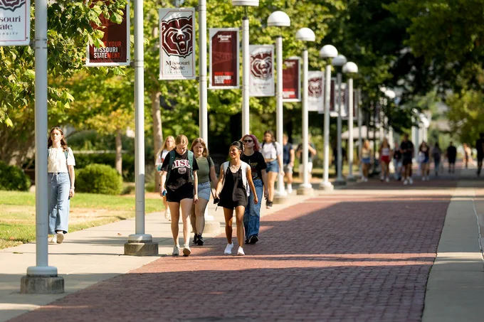 Group of students walking along a pathway lined with Missouri State University banners.