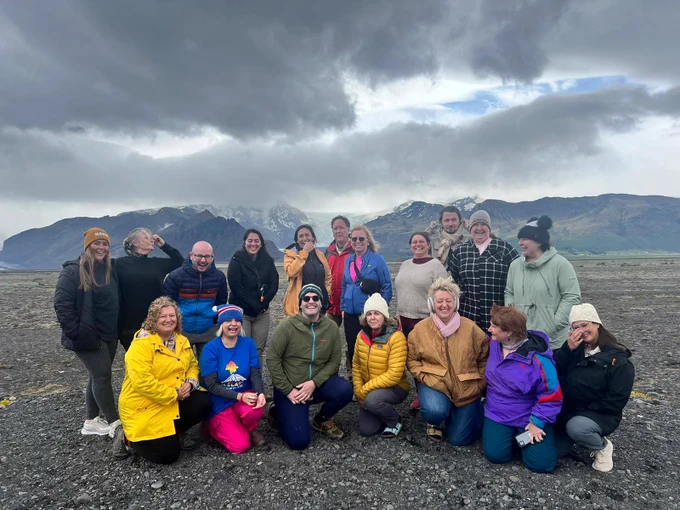 Group of people posing together in front of a scenic mountainous landscape, under a cloudy sky in Iceland.