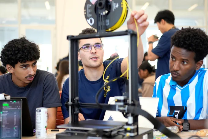 Three students sit at a table, as the middle participant reaches for the filament. (Photo by Adam Lau / UC Berkeley Engineering)