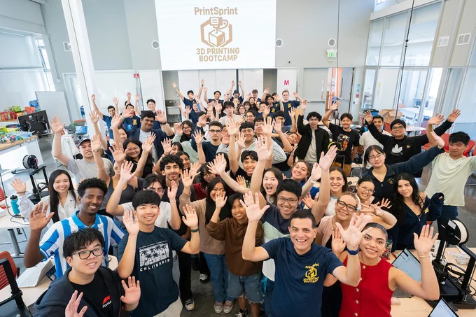 A wide group shot of participants each waving two arms in the air. The PrintSprint sign is posted on the wall above. (Photo by Adam Lau / UC Berkeley Engineering)