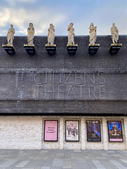The statues on Glasgow’s Citizens Theatre seen against a pale blue sky in the early morning autumnal light. The new facade of the Citizens Theatre is composed of a mass of black brick floating over a pale cream brick base with niches for posters of shows. The Citizens Theatre name is picked out in neon tubing. Appropriately for a theatre, the statues represent the Muses and are the four Greek goddesses Melpomene (tragedy), Thalia (comedy), Euterpe (song and poetry), and Terpsichore (dance). They are framed by William Shakespeare and Robert Burns. The statues were by the great Glasgow sculptor John Mossman best known for established the Glasgow School of Art. Though the Muses were originally from a building on Ingram Street they have now been on this site for 147 years having been brought here by the great Glasgow builder John Morrison who later built the City Chambers. As part of the work to regenerate the Citizens Theatre they were restored by Scottish sculptor David J Mitchell