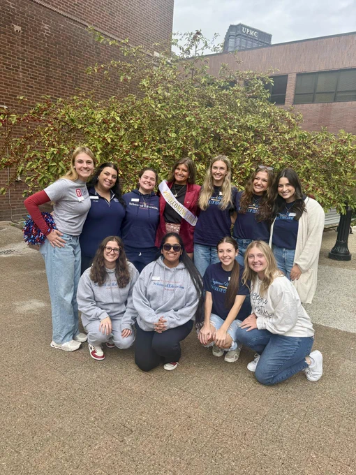 11 female students pose for a group photograph outside of Duquesne's School of Education. They are all wearing SoE merchandise, and one is wearing a Homecoming Court sash.