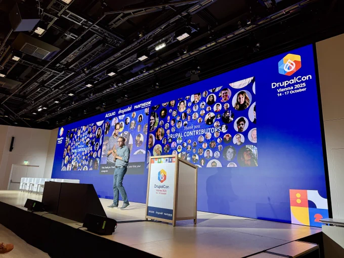 Dries presenting on stage at DrupalCon Vienna 2025 with a large screen showing a thank you message to Drupal contributors.