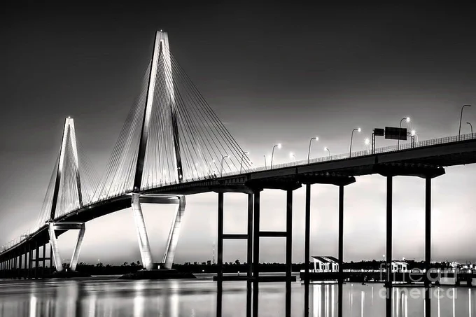 Black-and-white photograph of Arthur J. Ravenel Bridge in Charleston SC at night, with illuminated cables and shimmering water reflections. From the Fine Art Gallery of Shelia Hunt.