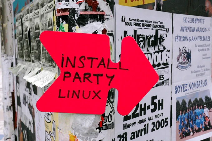 A bright red arrow-shaped sign reads “Install Party Linux,” taped to a wall covered with overlapping event posters and flyers.