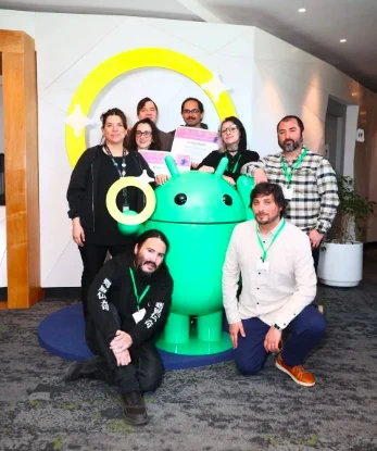 Una foto grupal de ocho personas posando sonrientes alrededor de una gran estatua verde del robot de Android. Algunos de ellos son representantes de las empresas Niebla Games y Octeto Studios, junto con Daniel Trocoli y Carmina Hernández.