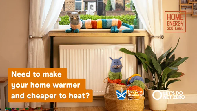 The text overlay on the image reads: ‘Need to make your home warmer and cheaper to heat?’. A colourful, knitted cat draught excluder is laid out on a windowsill between two white curtains. Beneath the windowsill, a caterpillar draught excluder sits in a woven basket on the wooden floor, beside a green potted houseplant.