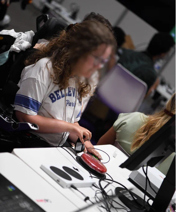 Venez tester sur le stand CapGame des setups adaptés permettant à tous de jouer. On voit une jeune fille en fauteuil électrique en train de jouer avec des contacteurs et un joystick adapté.