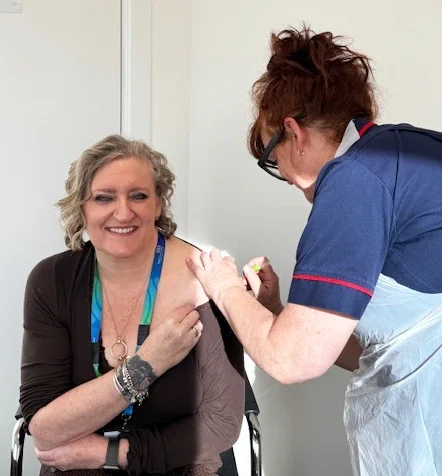 A photo of Dr Jane Padmore, Chief Executive at Sussex Partnership, sitting in a chair having her flu vaccination by a nurse