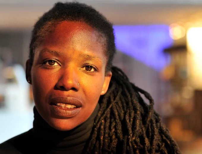 Photo of Kat François. She is looking directly at the viewer with a gentle smile. Her long dreadlocks are placed over one shoulder. She is wearing a black polo neck.