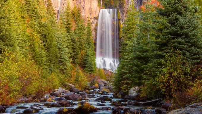 Tumalo Falls near Bend Oregon photographed on an October morning shortly after sunrise, showing the 97-foot cascade of Tumalo Creek framed by autumn foliage in the Deschutes National Forest. The photographer last visited in 1999 with a 35mm film camera and was struck by the transformation—areas once sparse after the destructive fires of the 1970s and 1980s have regenerated into lush forest. The deciduous trees along the creek banks glow in gold and orange, contrasting with evergreens and dark volcanic rock. The composition captures both the power of the waterfall and the sense of renewal over two decades of regrowth. Processed for a subtle painterly effect, the image evokes the feeling of standing before a living work of art. It celebrates resilience, time, and nature’s ability to heal, portraying one of Oregon’s most beloved waterfalls in the soft light of a peaceful autumn morning.
