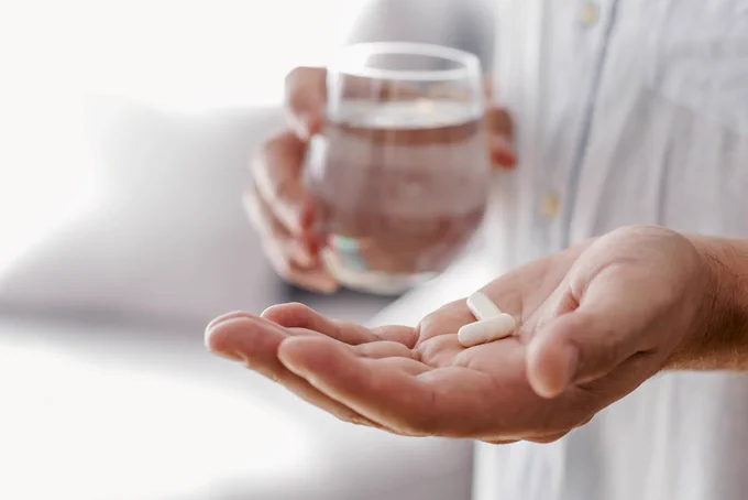 Close-up of a person taking a pill with a glass of water