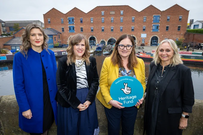 Four individuals standing by a canal with boats, holding a Heritage Fund sign, with Portland Basin in the background.