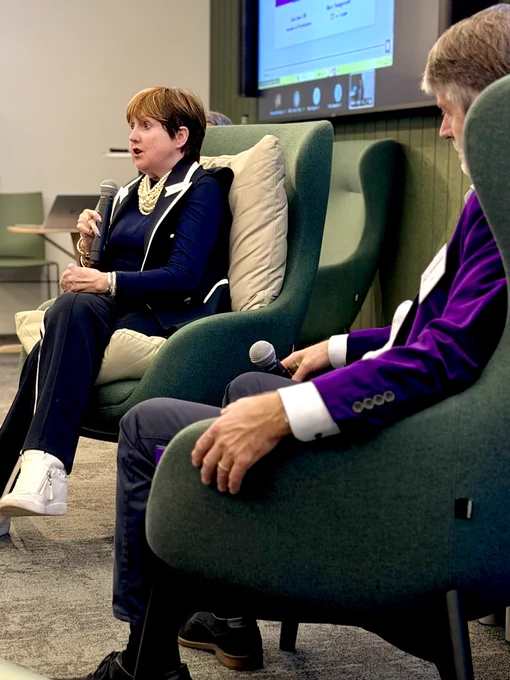 Kate is all in blue sat on a big comfy chair, Mark is partially obscured but you can see his purple jacket and white shirt cuffs. 