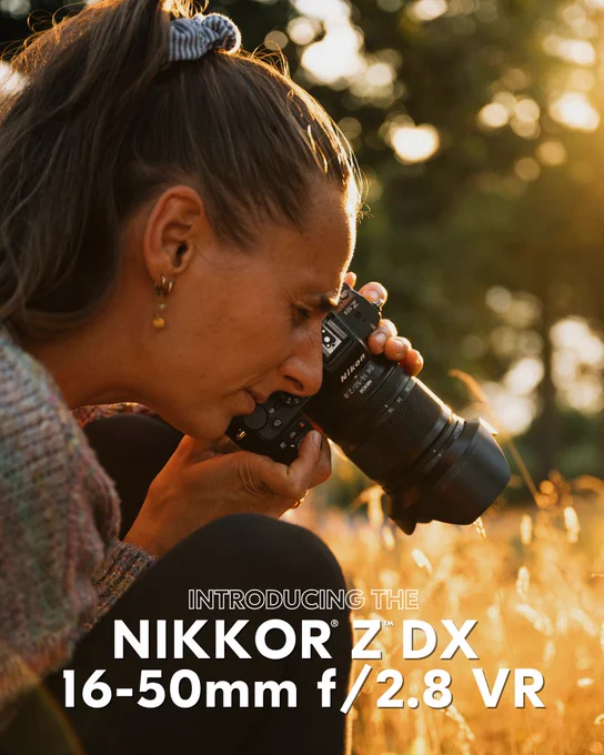 A photo of a woman holding a Nikon Z camera with the NIKKOR Z DX 16–50mm f/2.8 VR lens, crouched in golden sunlight while photographing a field of tall grass. Bold white text below reads: “Introducing the NIKKOR Z DX 16–50mm f/2.8 VR.”  