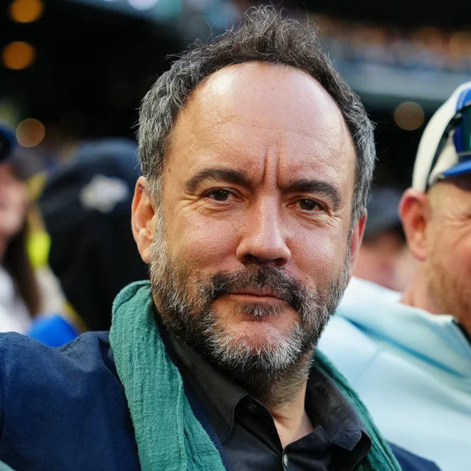 Dave Matthews sitting in the stands at T-Mobile Park. He's wearing a blue jacket and teal scarf.