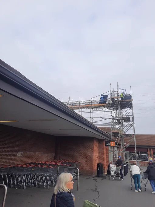 Scaffolding tower and worker carrying solar panels. 