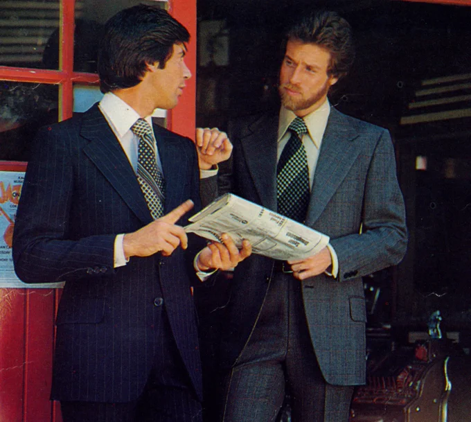 A 1970s photo showing two men in suits and wide ties talking about a newspaper