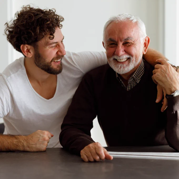 Father and son laughing together, one with an arm around the other. 
