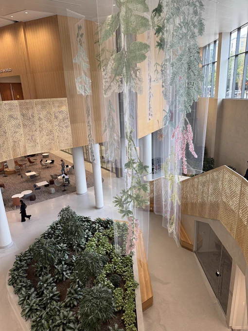 A staircase in the new School of Computer, Data & Information Sciences building at Wisconsin Madison. Tan wood structures surround tapestry art and a small indoor garden.