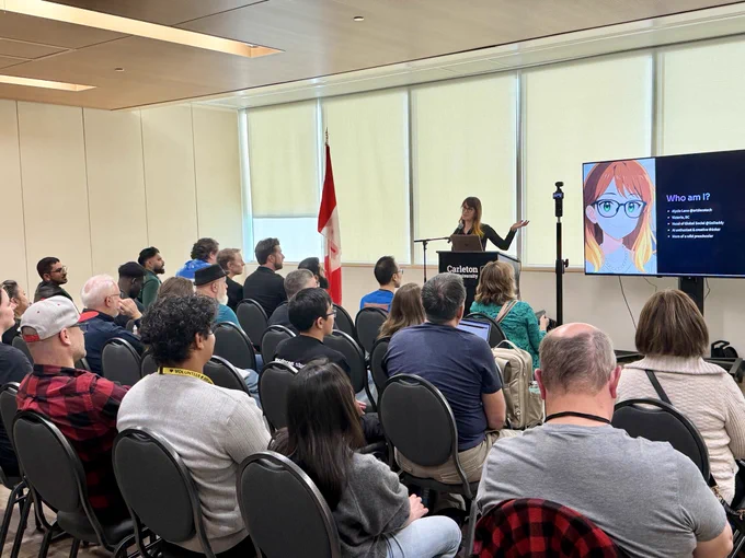 Alycia Leno speaks at WordCamp Canada, standing at a podium with a microphone in front of a large audience. A presentation slide beside her shows an illustrated avatar with orange hair and glasses under the heading “Who am I?” listing her roles, including “Head of Global Social @GoDaddy.” The talk takes place in a bright conference room at Carleton University, with a Canadian flag visible near the speaker.
