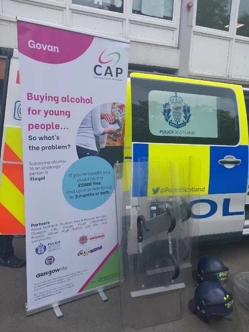 A banner for the Community Alcohol Partnership in front of a Police van, with Police shields and helmets.
