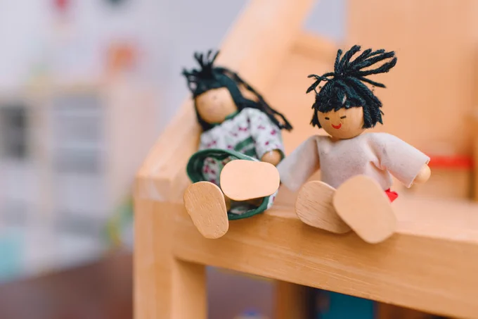 Two wooden dolls with yarn hair sitting on a small wooden bench, one lying down and one sitting upright.