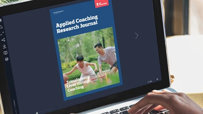 Laptop screen displaying an issue of "Applied Coaching Research Journal" , featuring an image of two individuals in a park.