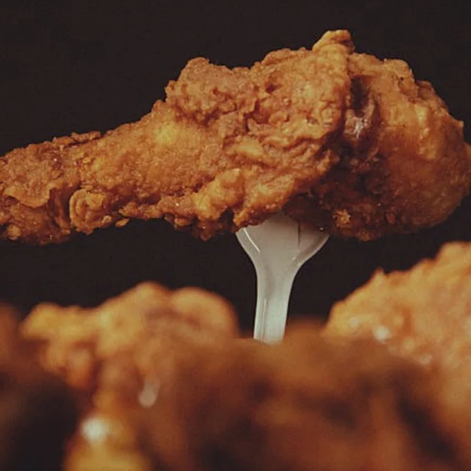 A close-up of a crispy fried chicken wing on a fork, highlighting its texture.