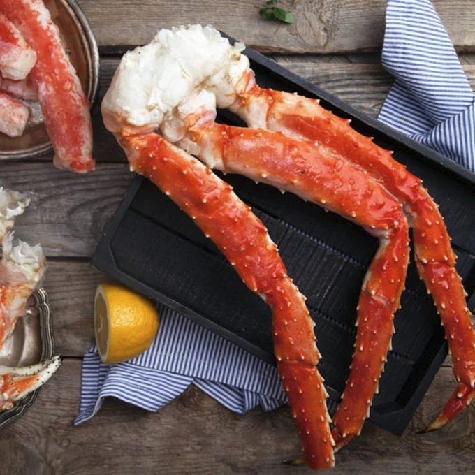 Delicious frozen and cooked King crab legs with lemon on a wooden background, ideal for seafood lovers.