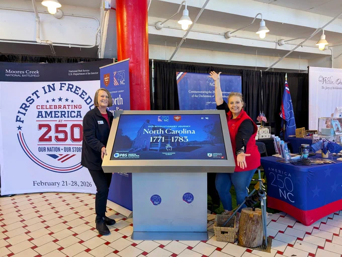 Two women stand next to an interactive display about North Carolina in the Revolutionary War. 