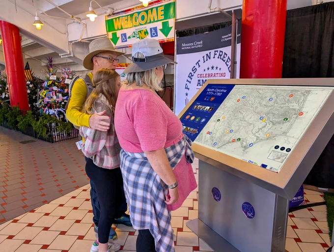 Three people look at an interactive display about North Carolina in the Revolutionary War. 