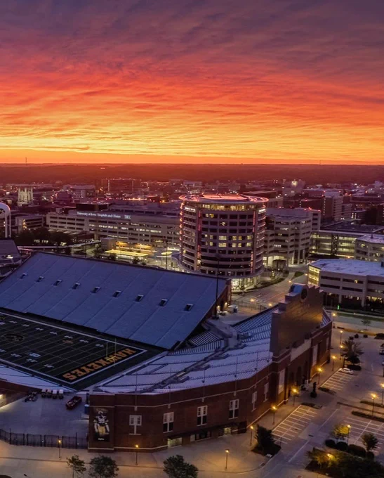 Aerial view of a kinnick stadium under a vibrant orange and purple sunset sky.
