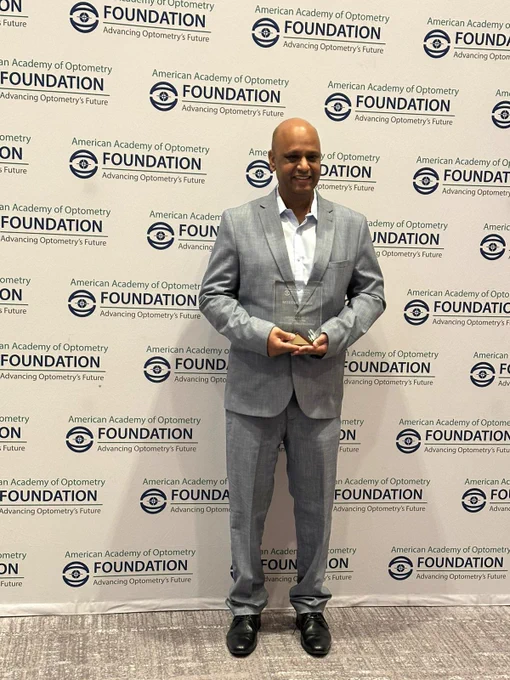 Phd candidate Mukesh Kumar standing in front of the American Academy of Optometry Foundation holding his Ezell Fellowship award.