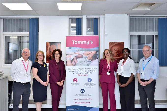 Group of five individuals standing beside a Tommy's promotional banner in a hospital setting.