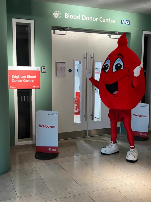 Billy Blood Drop mascot waves as he stands in front of the Brighton Blood Donor Centre entrance.